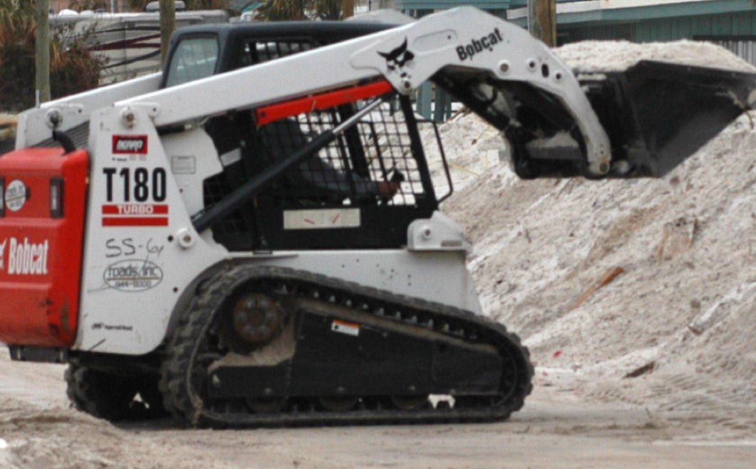 A compact skid-steer track loader moving material on a property